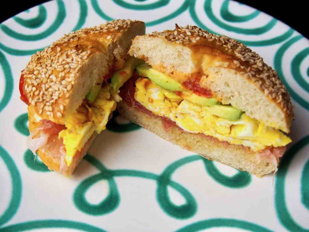 Frühstücksbagel mit Ei, Prosciutto, Avocado und Tomaten